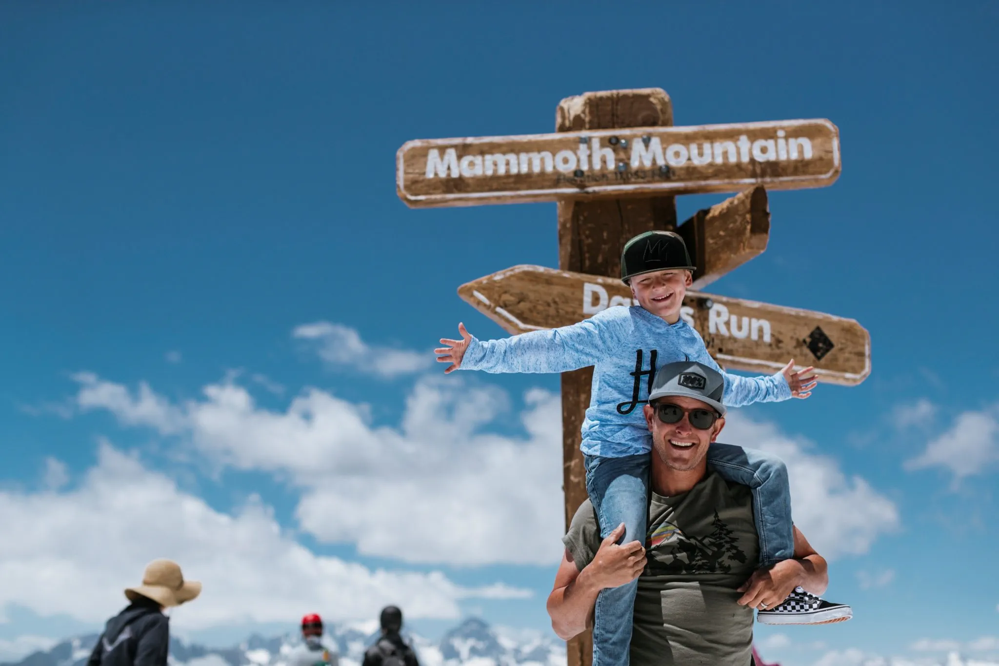 Kid sitting on dad's shoulder in front of the Mammoth Mountain wooden sign